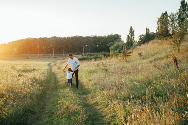享受英俊的爸爸带着他可爱的小儿子在绿草如茵的草地上玩耍孩子快乐妈妈