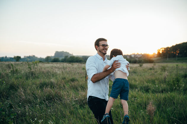女性英俊的爸爸带着他可爱的小儿子在绿草如茵的草地上玩耍爸爸男孩微笑