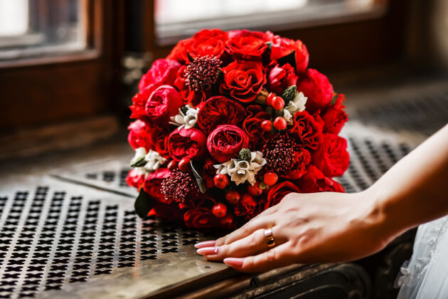 婚礼花束一个女人手旁窗台的格子上 摆着一束鲜艳的红色玫瑰和浆果的圆形新娘花束订婚细节新娘