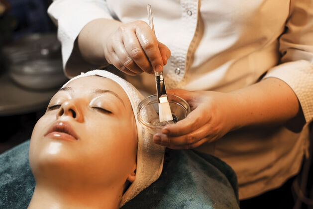 年轻化女性美容师手拿一碗透明质面膜 为以后的脸敷面膜在女性脸上过程水合手