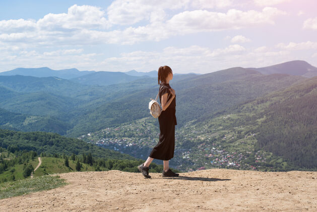 天空背着背包的女孩站在山上欣赏着视图.阳光天哪后方美丽假期