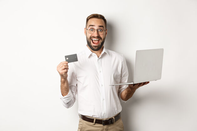 手势在线购物帅哥男子出示信用卡 用笔记本电脑在网上订购 站在白色背景上帅哥Person买家