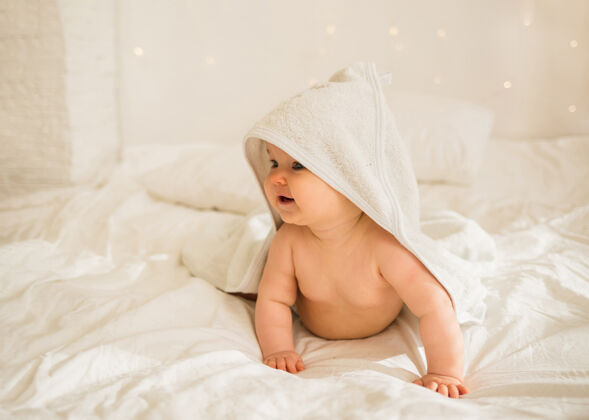 毛巾小女婴穿着白毛巾 头上戴着兜帽 四只脚躺在床上的白毯子上小卧室幼儿