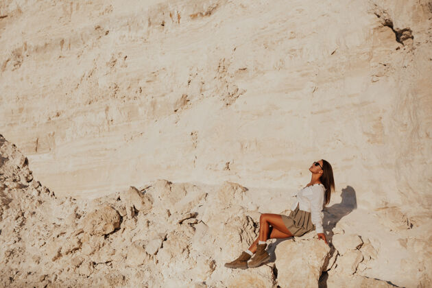 冒险戴着墨镜 穿着白衬衫 米黄色裙子和登山靴的女孩在白崖山上摆姿势极限复制空间健康