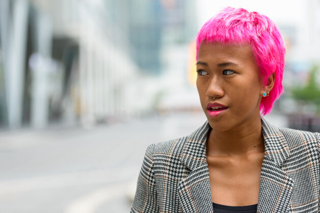 叛逆年轻叛逆的亚洲女商人的画像 粉红色的头发 在城市街道户外时髦思考城市
