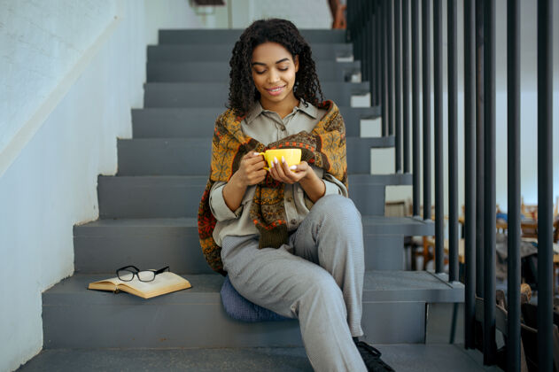 女孩坐在图书馆台阶上微笑着喝咖啡的女学生女咖啡馆用杯子 打开书和眼镜 教育和知识女孩在校园里学习人青少年坐着