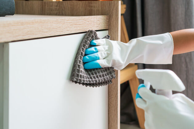 人主妇们手拿橡胶防护手套 用超细纤维布和清洁剂清洁客厅的橱柜表面清洁洗涤剂家庭主妇