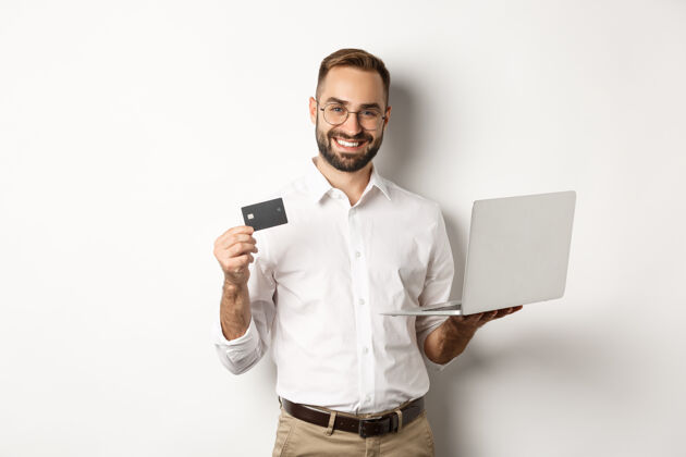成人在线购物帅哥男子出示信用卡 用笔记本电脑在网上订购 站在白色背景上BusinessManShirtShopping