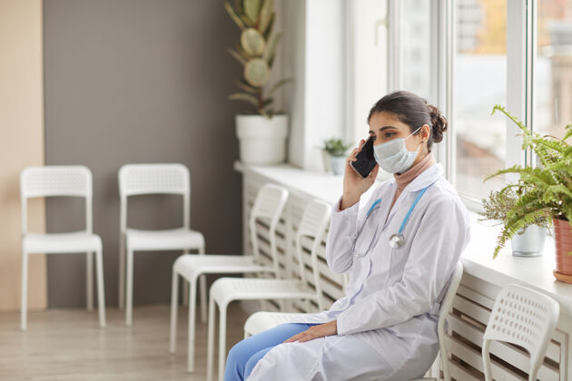 技术穿着白大褂 戴着防护面具的女医生坐在椅子上 拿着手机在医院里制服外科口罩表情