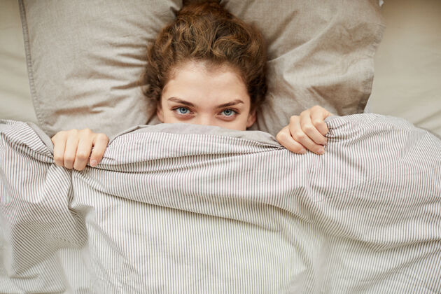 家庭房间高角度的年轻女子看前面躲在毯子下的床休息疲惫可爱