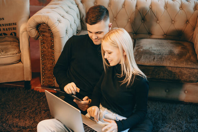 男人一对年轻漂亮的白人夫妇坐在地板上 看着笔记本电脑的屏幕笑着女朋友平板电脑移动