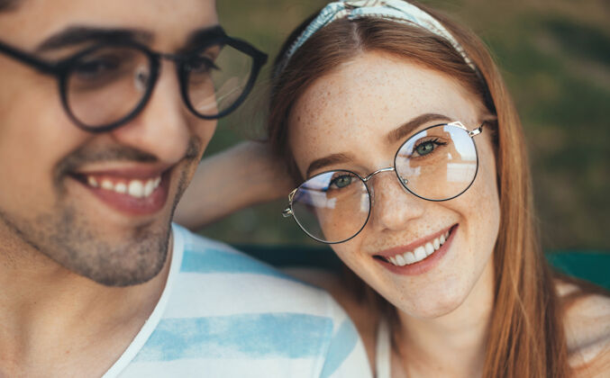 情人一个戴着眼镜的红发雀斑的可爱年轻女子的特写照片 在户外和她的男人坐在沙滩上微笑着订婚男人漂亮