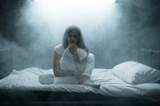 精神病疯狂的女人带着枕头坐在床上 黑暗的房间…迷幻的人每晚都有问题 抑郁和压力 悲伤 精神病院医院神秘人