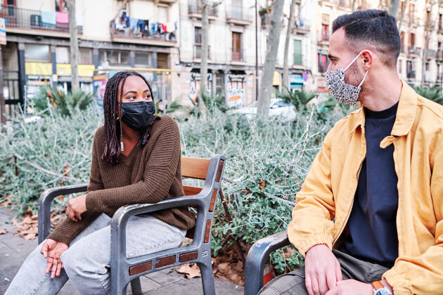 脸两个人戴着口罩坐在不同的椅子上保持距离户外.新正常生活方式.城市概念街道社会距离冠状病毒