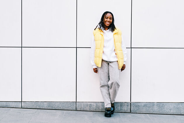 休闲一位年轻的非洲裔美国妇女一边靠在街上一边微笑着看着镜头墙.城市概念头发年轻人非洲