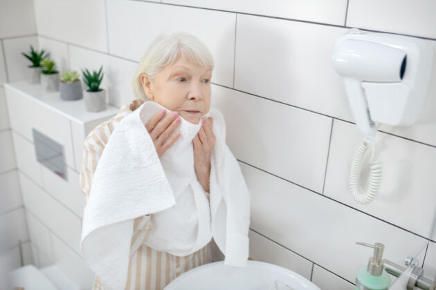 退休洗涤向上格雷-用毛巾擦干脸的头发女人家务老太太活跃的老年人