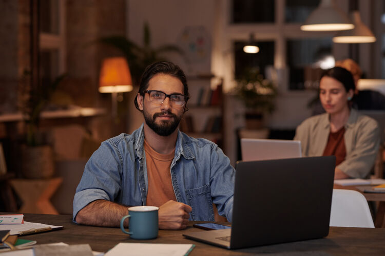 专业职业商人坐在办公室里拿着笔记本电脑 和同事们一起在墙上工作 看着前面的画像技术胡须成人