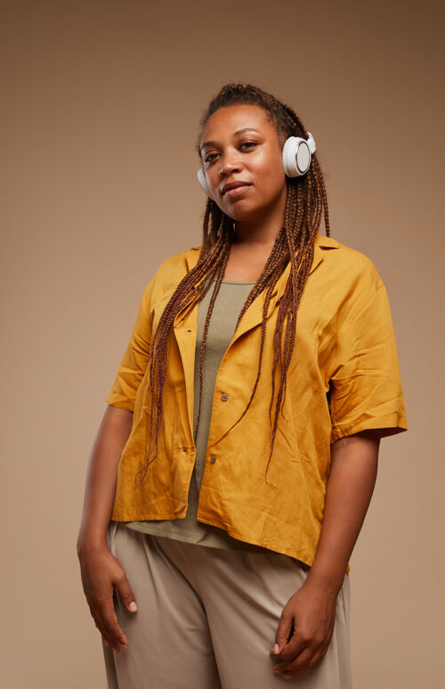 现代戴着耳机 穿着时髦衣服 在棕色背景上听音乐的时尚女性肖像音响设备时尚时髦