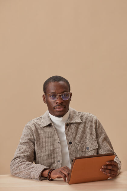 自信一个戴着眼镜的年轻人坐在桌旁看着面前的数字平板电脑专业职业西装严肃