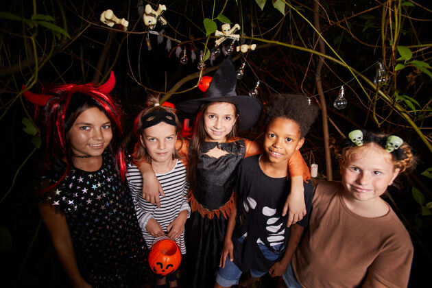 玩一群穿着盛装的快乐的孩子在黑暗的森林里对着镜头微笑 一起庆祝万圣节女巫幽灵十月