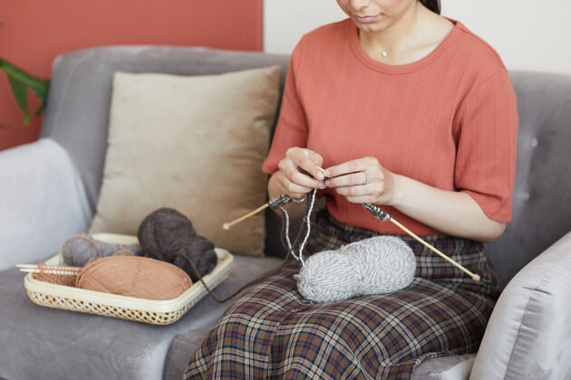 家庭房间坐在沙发上织围巾的女人的特写镜头针织针坐着成人