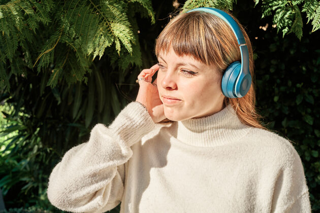 肖像一个漂亮的白人女孩在公园里戴着蓝色耳机听音乐姿势金发公园