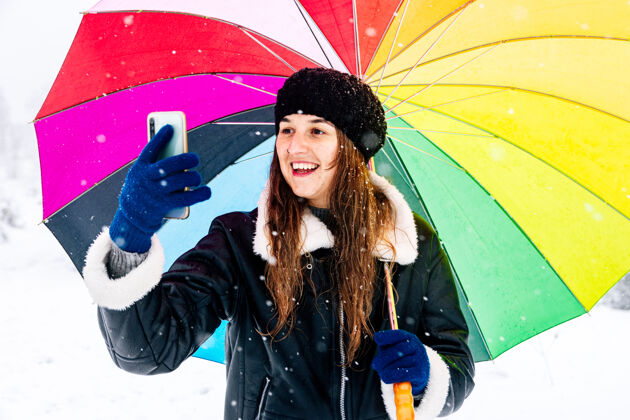冬季一个快乐的女人带着一把彩色雨伞在下雪时拍照的画像气象雷雨冰冻