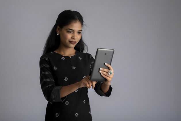平板电脑年轻的印度女孩用手机或智能手机上灰色微笑空白屏幕