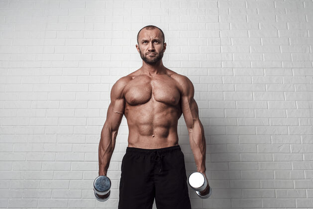 肖像健美运动员在砖墙上用哑铃练习二头肌锻炼质量腹部