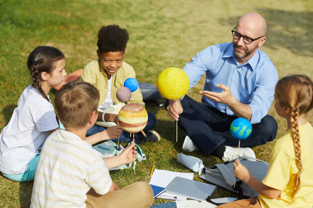 男生高角度的男老师指着行星模型 微笑着和一群孩子一起享受户外天文课 复制空间团体孩子天文学