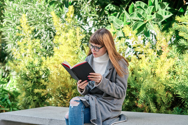教育一个蓝眼睛的白人金发女郎戴着眼镜在公园看书肖像女人书