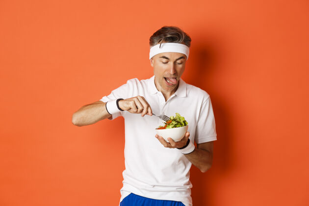 私人教练穿着运动服的有趣的中年运动员的肖像吃成熟沙拉