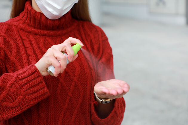 口罩不可辨认的女人戴着防护面具在城市街道喷洒洗手液酒精喷雾消毒剂卫生消毒