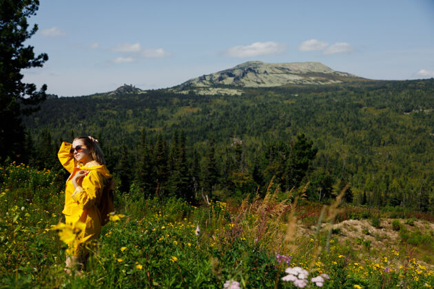 徒步旅行穿着黄色雨衣 背着背包的时尚潮人女人旅行者阿尔卑斯山阳光徒步旅行
