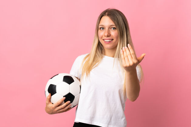 休闲一个年轻的金发女人拿着足球 在粉红色的地板上做着一个手势减肥足球时尚