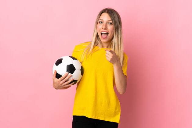 金发年轻的足球运动员女人孤立地用粉红色的手指指着你眼睛足球人