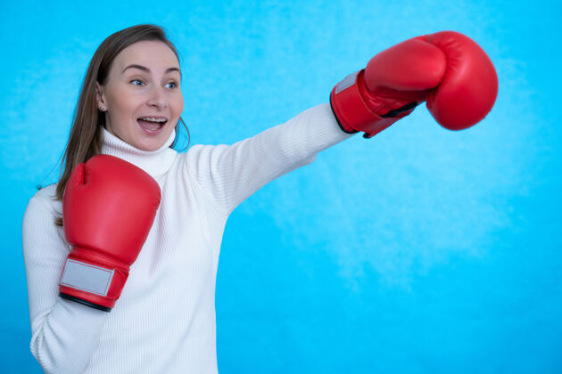 拳击戴着拳击手套的年轻女子拳击手在蓝色的墙壁上孤独地摆出尖叫的姿势拳击喊叫运动