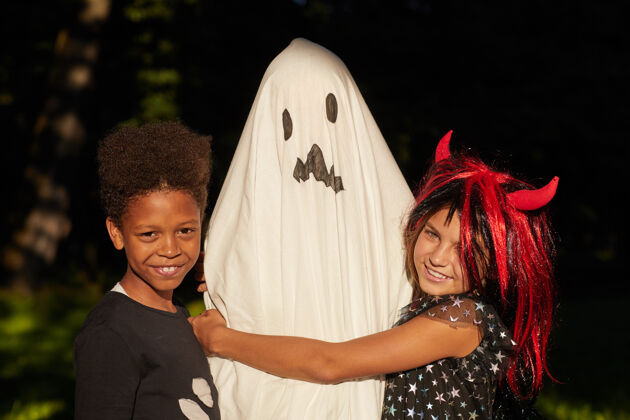 欢笑两个孩子在万圣节派对上穿着鬼衣拥抱他们的朋友的画像服装结合后代