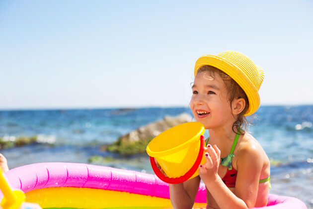 水处理戴着黄色草帽的女孩在沙滩上的充气游泳池里玩风 水和饮水机草帽帽子休闲