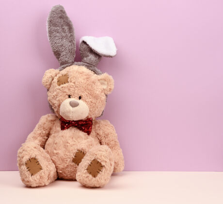 童年可爱的棕色泰迪熊头上戴着长耳朵的兔子面具 有趣的节日复活节贺卡木头熊小
