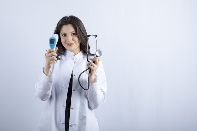 外套白墙上展示体温计和听诊器的女医生画像职业女人女孩