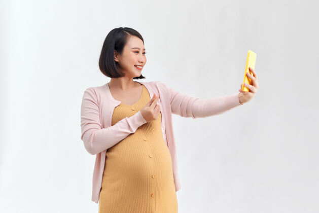 手机快乐的孕妇与智能手机采取自拍超过白色孕妇母亲手机