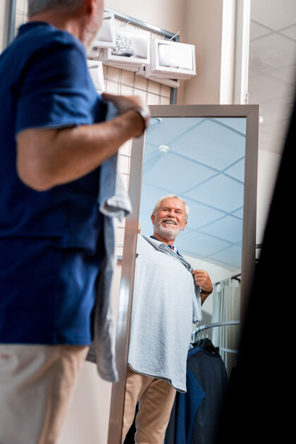 年龄一定要情绪激动的白发男人站在购物镜前 把灰色t恤放在胸前表示满意放松商业顾客