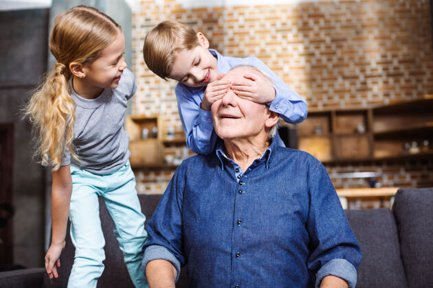 男性快乐的老人坐在沙发上 他的小孙子们闭上了眼睛孩子放松父母