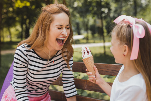 一起有趣的女孩金发有趣的女孩和她妈妈一起吃冰淇淋 她的鼻子上有一些冰淇淋收养微笑孩子