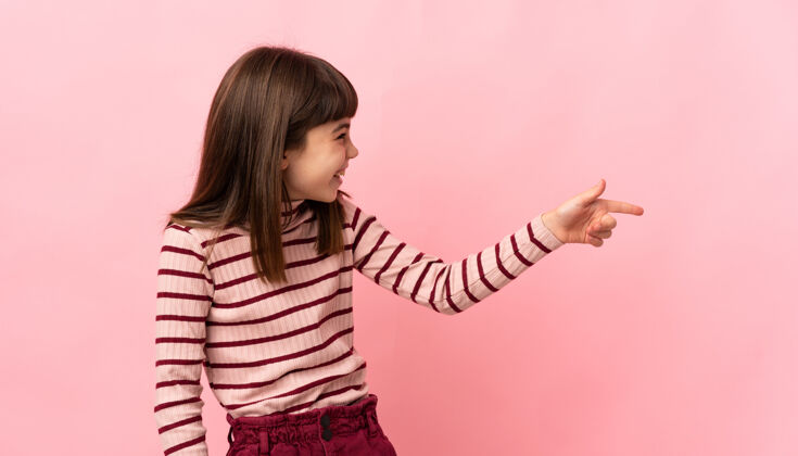 年轻小女孩孤立地站在粉红色的墙上 手指着侧面 展示着一个产品人女孩人