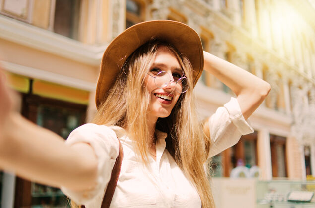 城市情绪化的金发女人戴着毡帽和眼镜自拍古城建筑采取城市景观周末