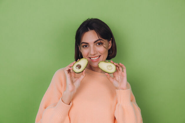 鳄梨年轻女子穿着休闲桃毛衣隔离在绿橄榄墙上捧着鳄梨 健康护肤理念 复制空间自然人漂亮