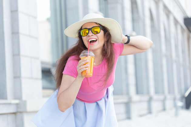 白种人一个戴着帽子 戴着眼镜 手里拿着果汁的开朗积极的年轻女子的肖像风格街道魅力
