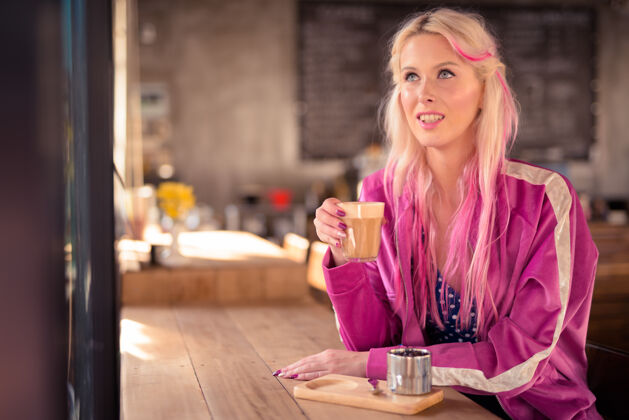 人快乐的年轻漂亮的金发女人在咖啡店思考和放松粉色态度现代
